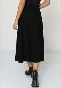 Jupe noire, mi-longue, avec une texture côtelée. Portée avec des bottines, présentant un détail de fermeture éclair. Design simple et fluide.