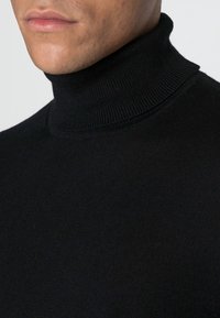 Zwarte coltrui met een geribbelde halslijn en een gladde textuur, voorzien van lange mouwen en een getailleerde silhouet.