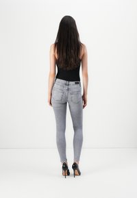 Grå denimjeans med middels livhøyde, to baklommer og en svak falming, sammen med svarte stiletthæler.