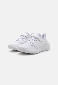 Chaussures de sport blanches avec une tige en mesh, une sangle réglable et une semelle en caoutchouc. Présentent trois bandes texturées sur le côté.