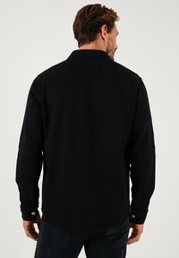 Camisa de algodón negra de mangas largas, con cuello de punta y puños abotonados. Tejido texturizado con un ajuste ligeramente holgado.