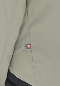 Ljusgrön isolerad jacka med en slät textur, försedd med en Primaloft-tag och rena sömmar. Designen är minimalistisk och funktionell.
