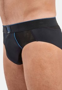 Svarta kalsonger med elastiskt midjeband, med meshsidor, kontrasterande blå sömmar och en logotyp på midjebandet. Mjuk tygstruktur.