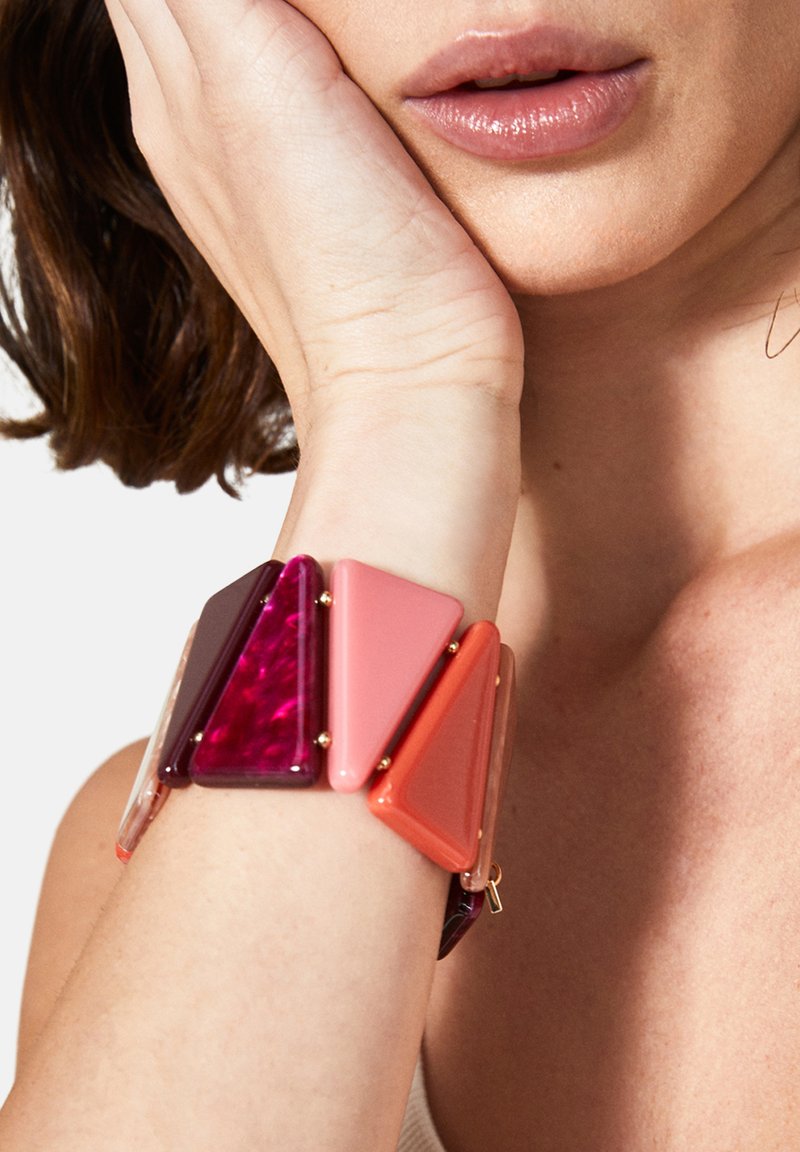 Bracelet en acrylique triangulaire multicolore présentant des nuances de rose, de violet et de rouge, avec des accents dorés et un design flexible.