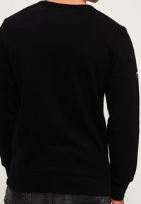 Pullover nero a maniche lunghe realizzato in tessuto morbido, con scollatura a girocollo e polsini a costine. Presenta un piccolo logo sul maniche.