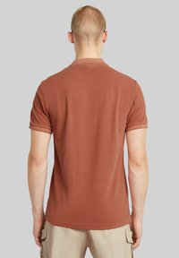T-shirt a maniche corte color ruggine realizzato in tessuto morbido; presenta una vestibilità classica e un colletto a coste, con una superficie liscia e senza motivi.
