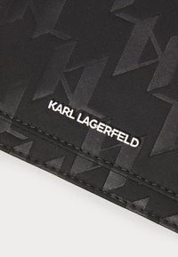 Tissu texturé noir présentant un motif géométrique et un logo embossé. "KARL LAGERFELD" en blanc en bas pour le contraste.