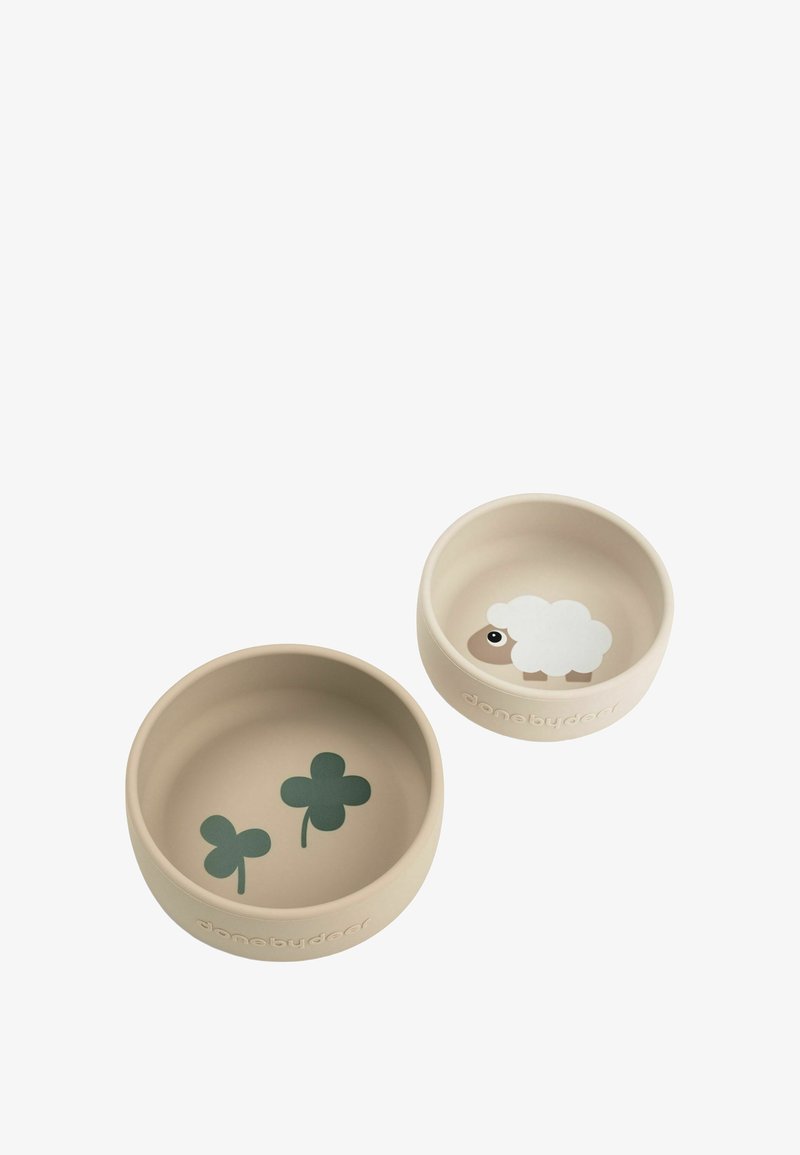 Deux bols beige en silicone, l'un orné de trèfles verts, l'autre d'un motif de mouton blanc. Les deux sont ronds avec une texture lisse.