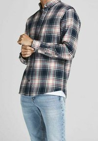 Camicia di flanella a quadri in blu navy, grigio e rosso. Presenta un colletto con bottoni e maniche lunghe, abbinata a jeans azzurri.