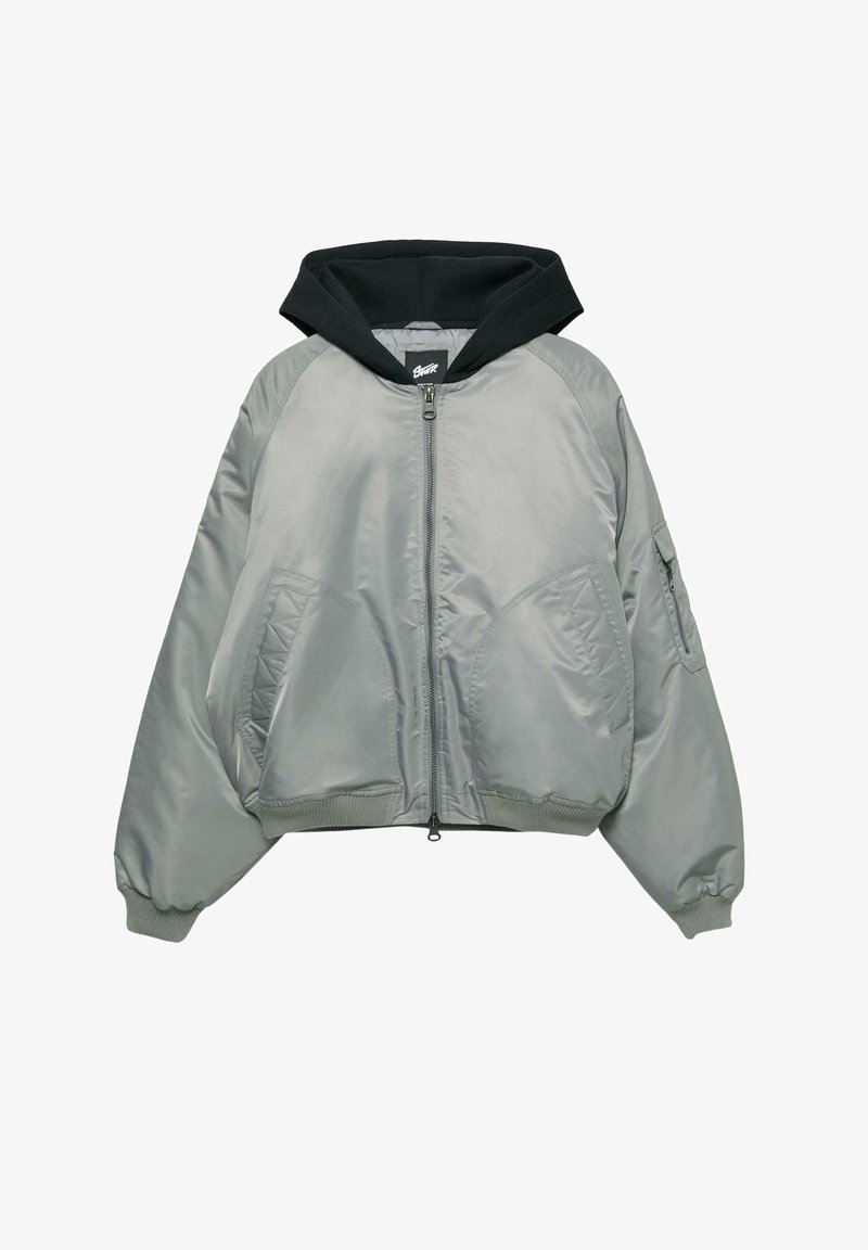 Szara kurtka bomber z czarnym kapturem, zamek błyskawiczny, ściągacze przy rękawach i dwie przednie kieszenie. Charakteryzuje się gładką, błyszczącą teksturą i pikowanymi akcentami.