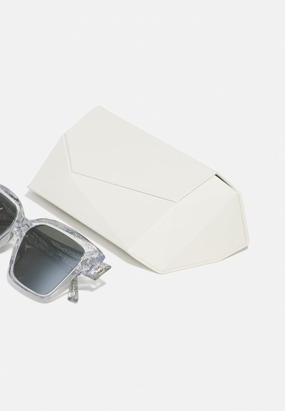 Ochelari de soare cu rame transparente și lentile gri în gradient, alături de un toc geometric alb cu închidere prin clapetă și suprafață texturată.