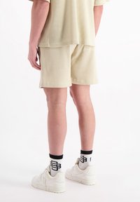 Beige geribbelde top met korte mouwen gecombineerd met bijpassende shorts. Persoon draagt witte sneakers en zwart-witte gestreepte sokken.