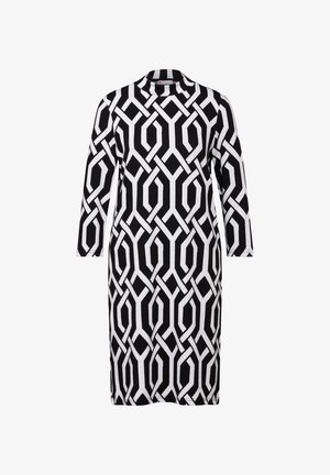 Czarna i biała sukienka do kolan z długimi rękawami, wysokim dekoltem i wyraźnym geometrycznym wzorem wplecionych ze sobą łańcuchów.