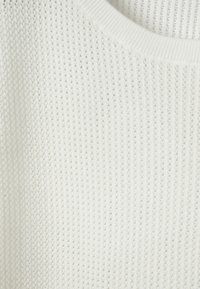 Gros plan sur un tissu blanc en maille avec un petit motif gaufré régulier et un col rond côtelé.