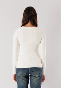Top a maniche lunghe bianco a coste con scollatura tonda e silhouette aderente, abbinato a jeans in denim blu.