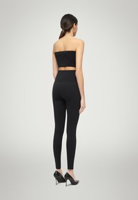 Zwart strapless top met bijpassende high-waisted legging, gemaakt van een glad, rekbaar materiaal. Gecombineerd met zwarte hoge hakken.
