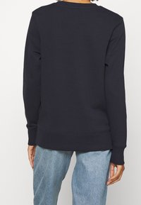 Donkerblauwe sweatshirt met ronde hals, geribbelde manchetten en zoom, gemaakt van zachte stof. Gecombineerd met lichtblauwe spijkerbroek.