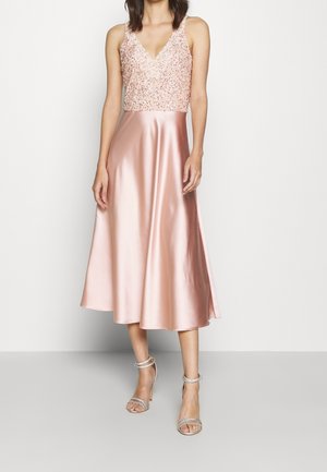 Ærmeløs lyserød satin kjole med paliet-pyntet krop, V-udskæring og A-line midilang nederdel, båret med sølvfarvede hæle med anklerem.