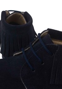 Stivaletti alla caviglia in suede navy con dettaglio di frange e lacci navy. Fodera interna morbida e cuciture decorative visibili. Design con punta rotonda.