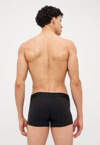 Schwarze Boxer-Shorts mit tailliertem Schnitt und elastischem Bund, hergestellt aus einem glatten, dehnbaren Material, von hinten präsentiert.