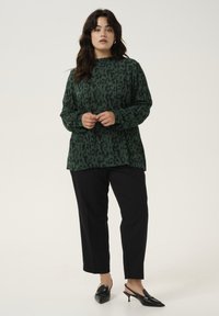 Green patterned long-sleeve top with a relaxed fit, paired with black tapered pants and black pointed-toe heels. Simple design, smooth texture.