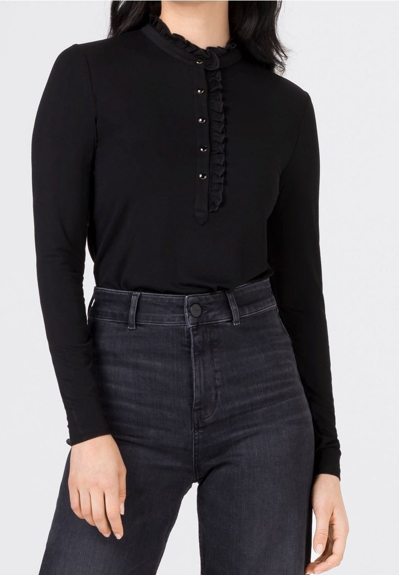 Haut noir à manches longues avec un col à volants, doté d'une patte de boutonnage et en tissu doux et lisse, associé à un jean foncé taille haute.