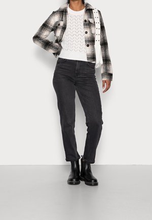 Giacca a quadri in bianco e nero con colletto, maglione di maglia bianco, jeans neri slim e stivaletti neri alla caviglia. Porta una borsa bianca.