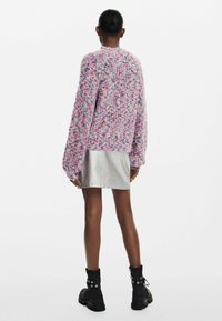 Sweter dzianinowy w pastelowym różu z kolorowymi plamkami, w luźnym kroju, z długimi rękawami, zestawiony z błyszcząca srebrną spódnicą i czarnymi botkami za kostkę.