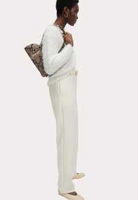 Pull blanc duveteux, pantalon crème, ballerines beige et sac à motif crocodile. Silhouette définie avec des matériaux texturés et des tons neutres.