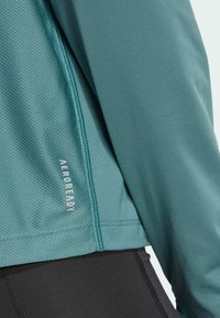 Teal athletic top with textured mesh panel, featuring a smooth fabric, flat seams, and “AEROREADY” logo on the lower right side.