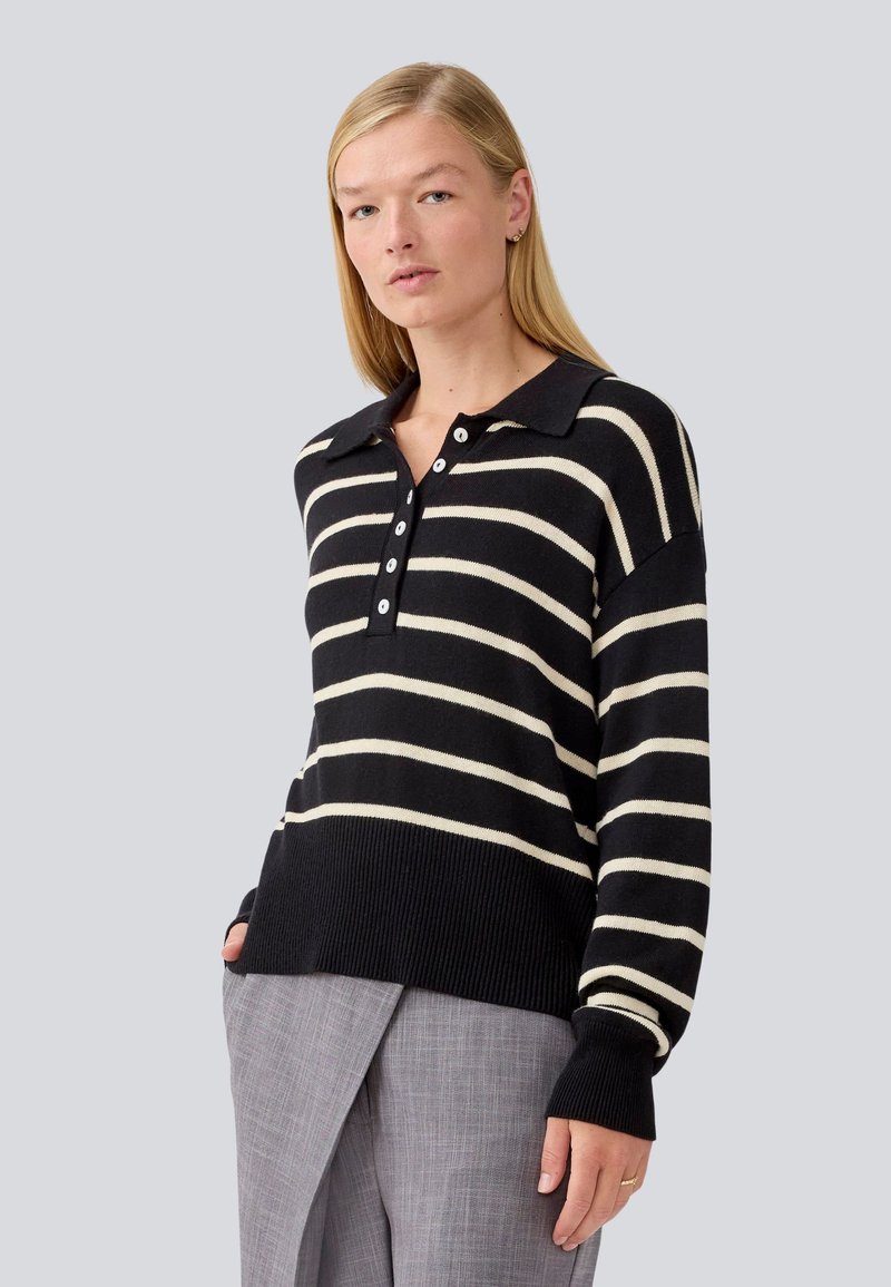 Pull en maille rayé noir et crème avec un col, des manches longues et un ourlet côtelé. Associé à un pantalon texturé gris.
