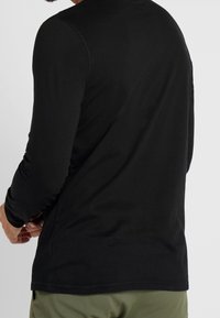 Czarny t-shirt z długim rękawem wykonany z miękkiego materiału, z okrągłym dekoltem i bezszwowym designem, z minimalnymi detalami szwów.