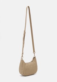 Beige quilted crossbody bag with a curved shape, adjustable strap, zipper closure, and diamond pattern detailing. Smooth synthetic material.