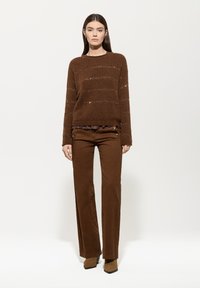 Brown knit sweater with horizontal stripes and metallic accents, paired with brown wide-leg trousers and brown heeled ankle boots.