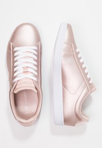 Metallic rose gold sneakers with white laces, smooth texture, and a low-top design, featuring a white rubber sole and subtle branding.