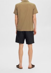 Kortärmad khakiskjorta, texturerad tyg; kombinerad med svarta shorts, avslappnad passform, ovan knä-längd. Buren med bruna slidesandaler.