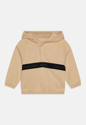 Felpa beige realizzata in tessuto morbido, con un'apertura frontale a bottoni, una banda orizzontale nera con la scritta "Calvin Klein Jeans" e polsini a coste.