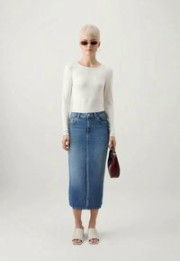 Top leveiro branco de manga longa combinado com uma saia lápis de ganga, sandálias bejes, óculos de sol oversized e uma mala bordeaux.