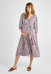 Blumiges Wickelkleid aus leichtem Stoff, mit V-Ausschnitt, Dreiviertelärmeln, einem Bindegürtel und bunten Blumenmustern auf blauem Hintergrund.