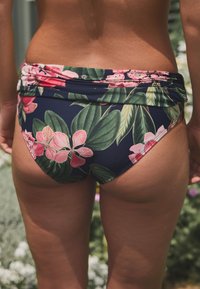 Gėliniai bikini kelnaitės su tamsiai mėlynu fonu, ryškiai rožinėmis gėlėmis ir žaliais lapais. Lygus audinys su raukšlės juosmens detale.