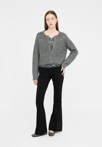 Cardigan corto grigio con motivo testurizzato e dettagli con bottoni, indossato sopra una maglietta nera con stampa animalier, abbinato a pantaloni neri a zampa d'elefante e ballerine.
