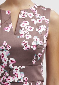 Brun udenærmet kjole med V-udskæring, prydet med et blomsterprint i pink og hvidt med grønne accenter. Glat stofoverflade.