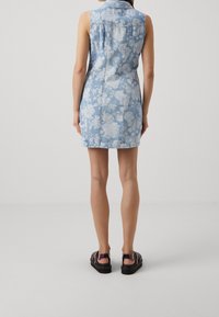 Denim dress in light blue with floral pattern, sleeveless design, fitted silhouette, and mid-thigh length, paired with black sandals.