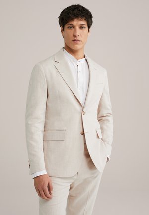 Light beige linen suit with a single-breasted jacket, two front pockets, and matching trousers. White collared shirt visible underneath.