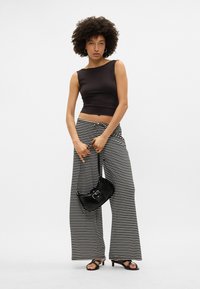 Top de tanque preto cropped, calças largas preta e branca com riscas, mala preta com fivela ao ombro, sandálias pretas com tiras no tornozelo.