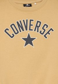 Sinepju dzeltena siltā krekls ar "CONVERSE" tekstu un melnu zvaigznes grafiku. Mīksta auduma, ar apaļu kakla izgriezumu un ribinātām piedurknēm.