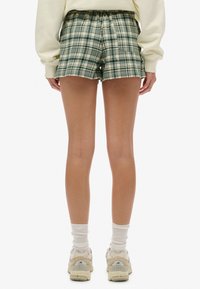 Pantalones cortos a cuadros verdes y blancos con cintura elástica, dos bolsillos laterales y un corte relajado. Se llevan con zapatillas deportivas beige claro y calcetines blancos.