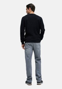 Suéter de punto azul marino oscuro con cuello redondo, combinado con unos vaqueros de denim gris claro. Los vaqueros tienen bolsillos traseros y un corte relajado.