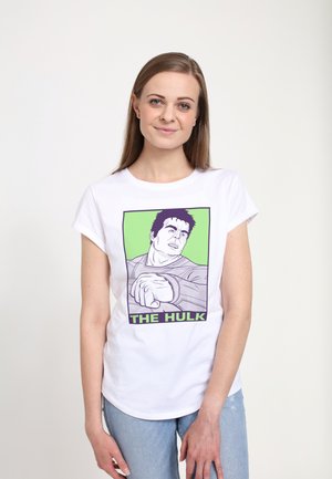 Hvid t-shirt med en trykt illustration af en karakter med mørkt hår. Designet inkluderer grønne og lilla accenter samt teksten "THE HULK".