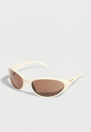 Occhiali da sole avvolgenti color crema con lenti marroni e logo "ARNETTE" sulla stanghetta, esposti su una superficie bianca.